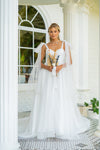 The Nicola is a superb A-line wedding gown with tulle bow straps. A corsage that features a sweetheart neckline with invisible zip closure at center back. Small bows with long ribbons that are made of veiling draw attention. The luxurious skirt is made of several layers of veiling that passes into a long train. 