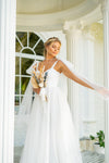 The Nicola is a superb A-line wedding gown with tulle bow straps. A corsage that features a sweetheart neckline with invisible zip closure at center back. Small bows with long ribbons that are made of veiling draw attention. The luxurious skirt is made of several layers of veiling that passes into a long train. 